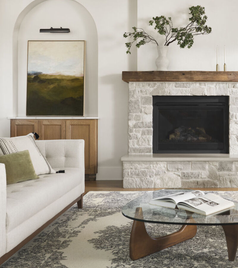 half of a living room with an ivory couch, a glass coffee table, and a grey brick fireplace